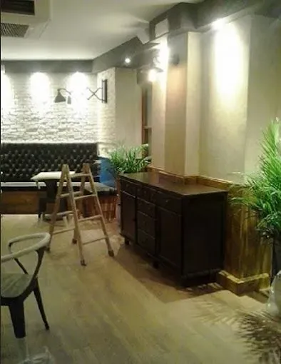 Interior con poca luz, suelo de madera, apliques de pared, armario oscuro, plantas en macetas, escalera y zona de bar.