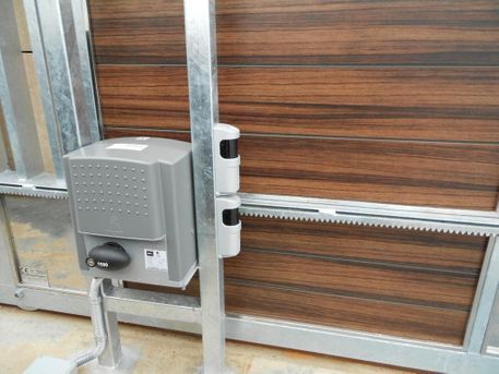 Puerta corredera automática con motor y sensores de seguridad. La puerta tiene paneles marrones y marco metálico gris.