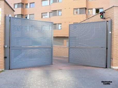 Puertas metálicas grises, abiertas, que dan a la entrada de un edificio de ladrillo. Un semáforo se divisa arriba.