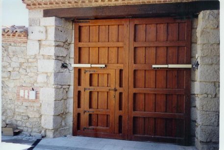 Puertas dobles de madera enmarcadas en una entrada de piedra. Puertas marrones con vigas horizontales y verticales.