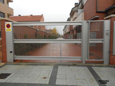 Puerta metálica sobre pilares de ladrillo que bloquea una calle adoquinada frente a edificios residenciales. Señal de 