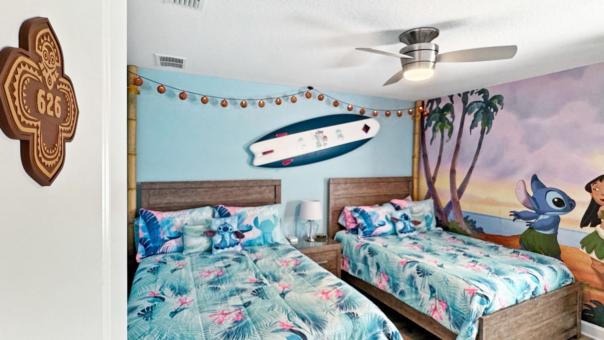 A stitch themed bedroom with two beds and a surfboard on the wall.