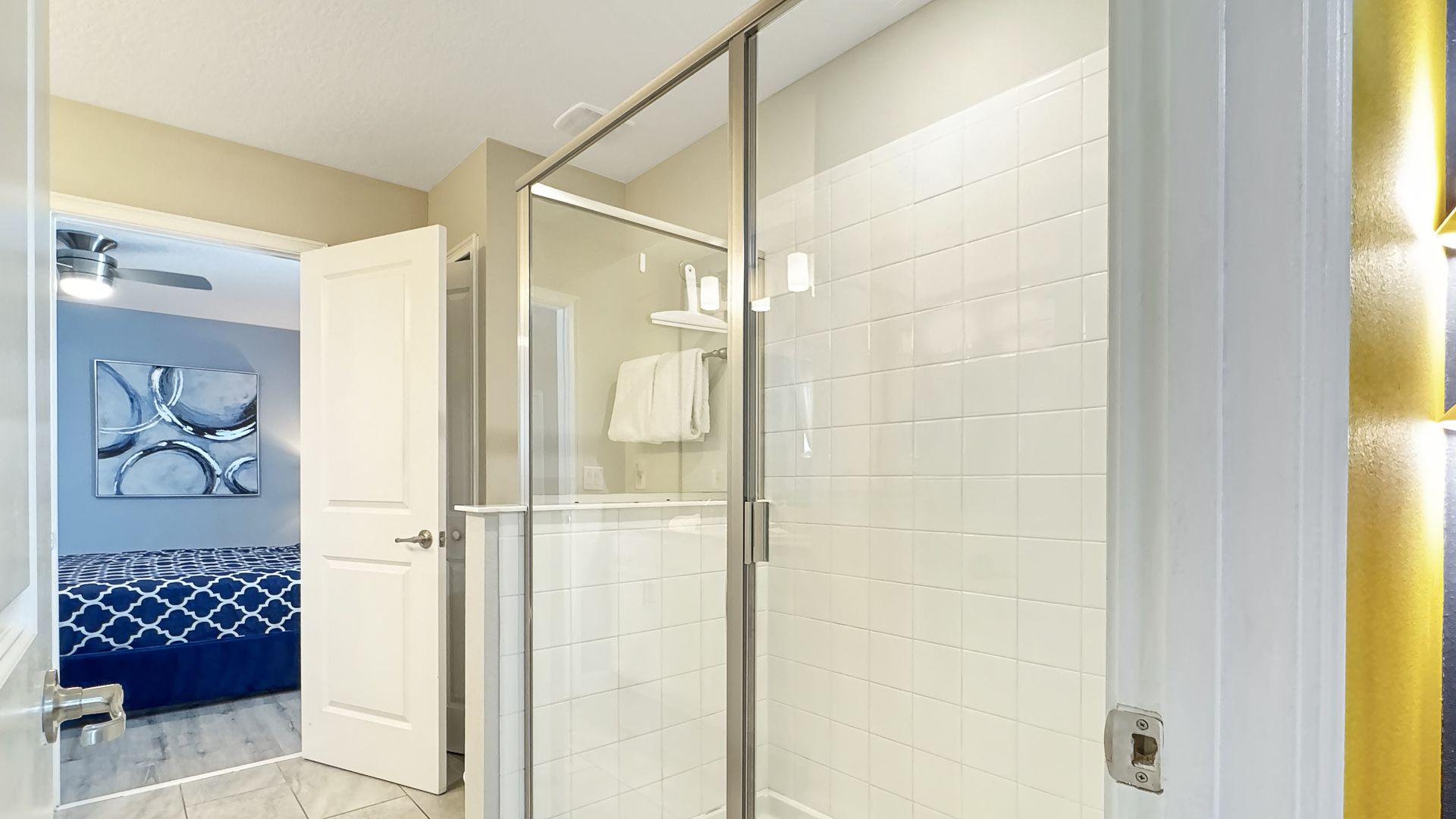 A bathroom with a walk in shower and a bedroom in the background.