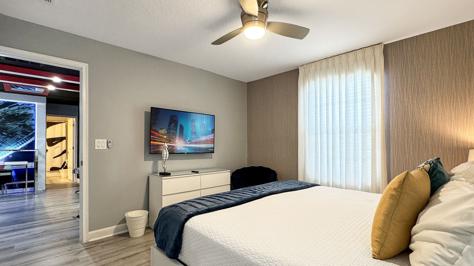 A bedroom with a king size bed , television , dresser and ceiling fan.