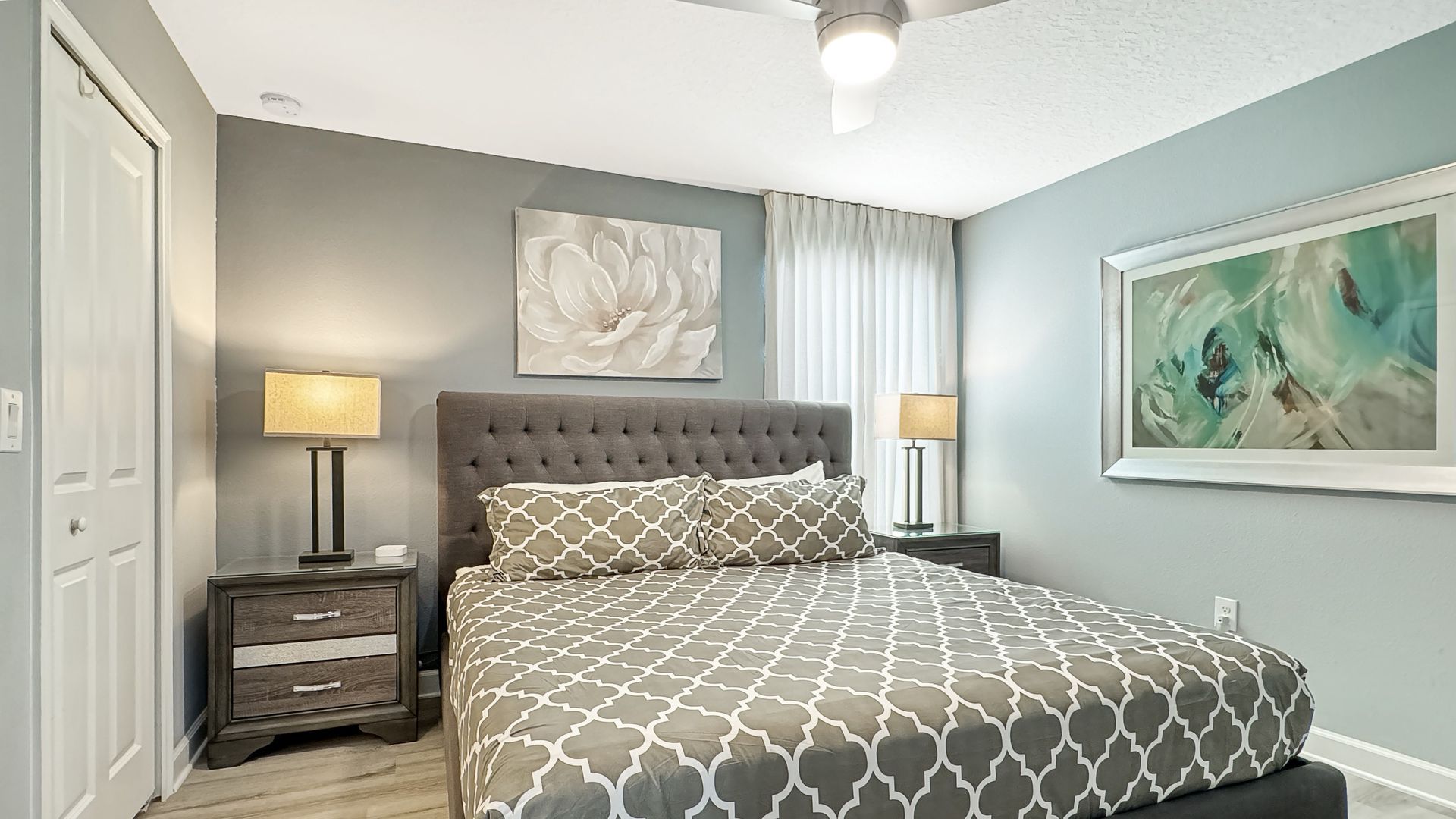 A bedroom with a king size bed , nightstands , lamps and a ceiling fan.