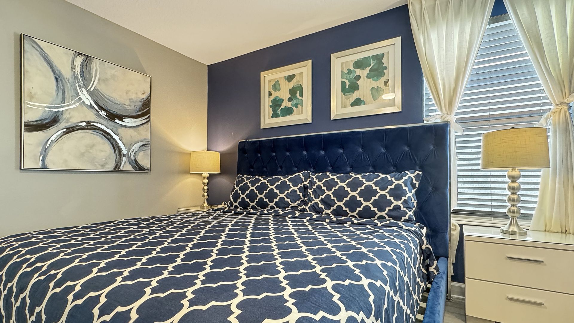 A bedroom with a king size bed , two lamps , a nightstand and a window.