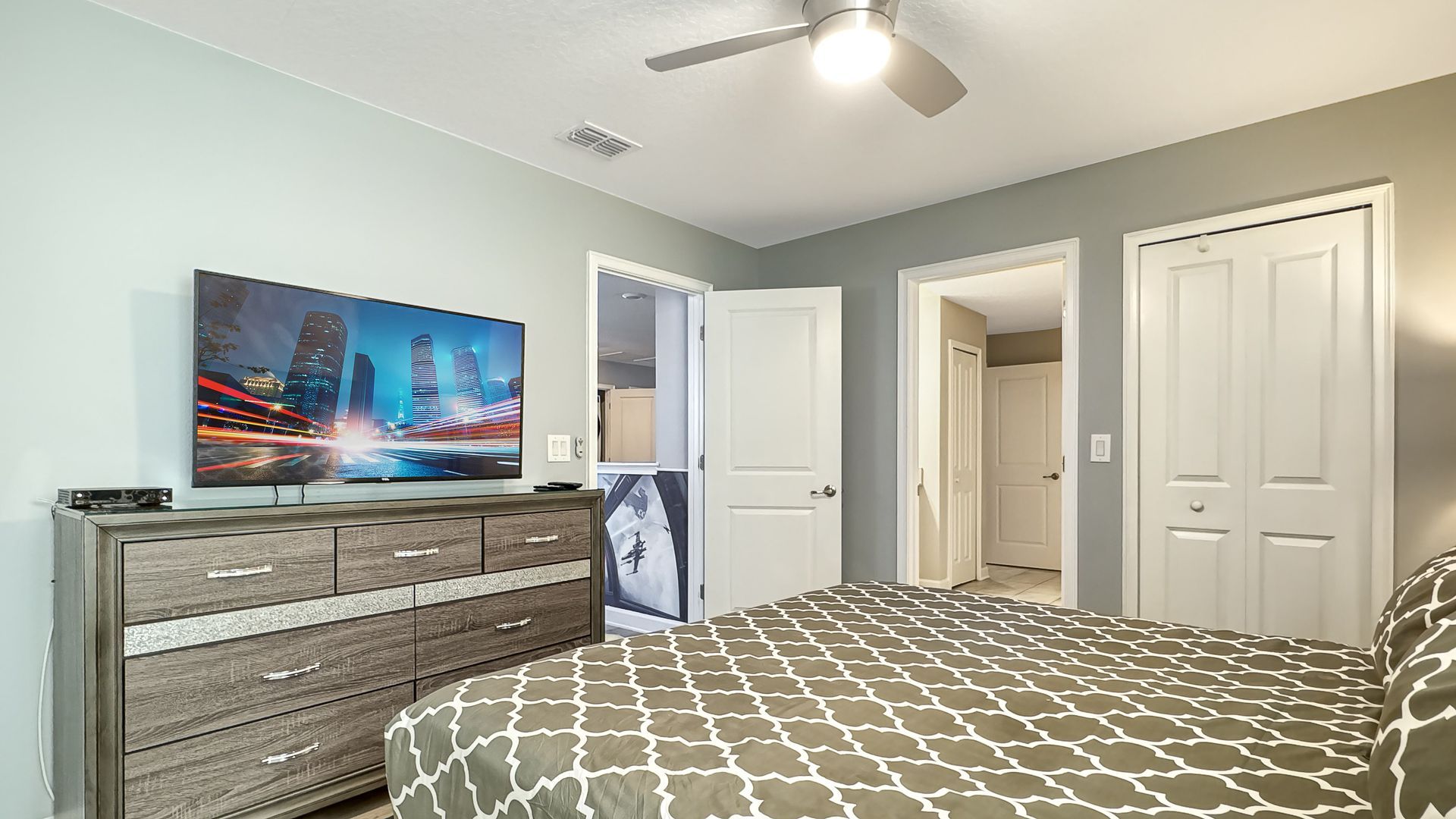 A bedroom with a bed , dresser , television and ceiling fan.
