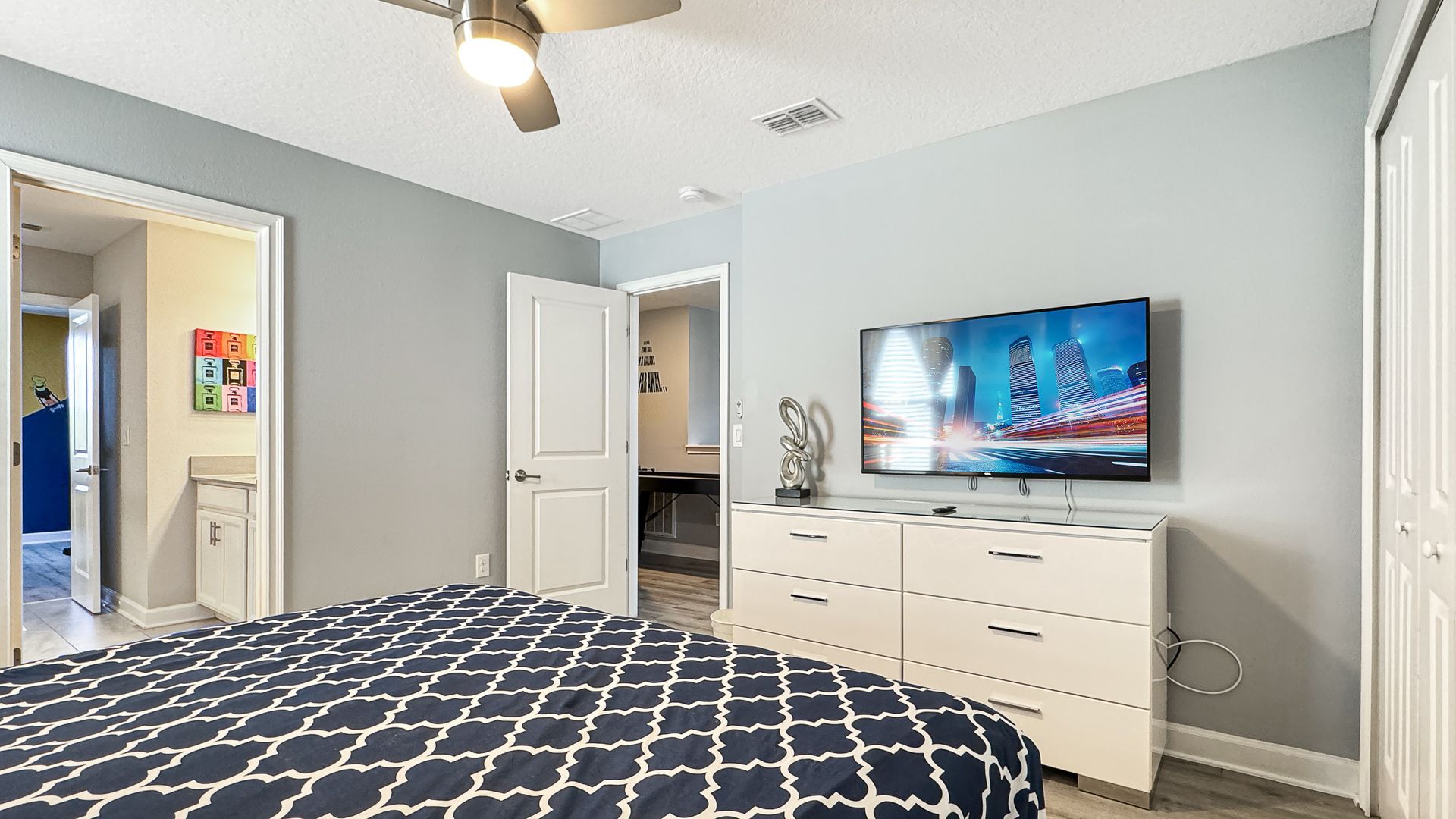 A bedroom with a bed , dresser , television and ceiling fan.
