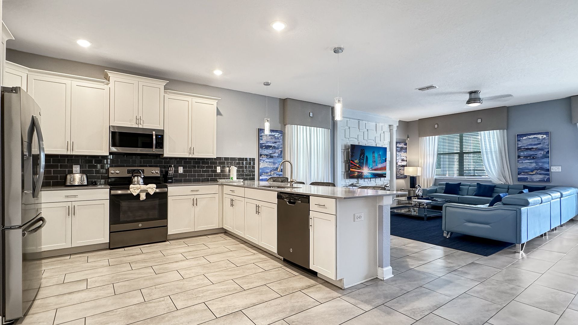 A kitchen with white cabinets and stainless steel appliances and a living room with blue couches.