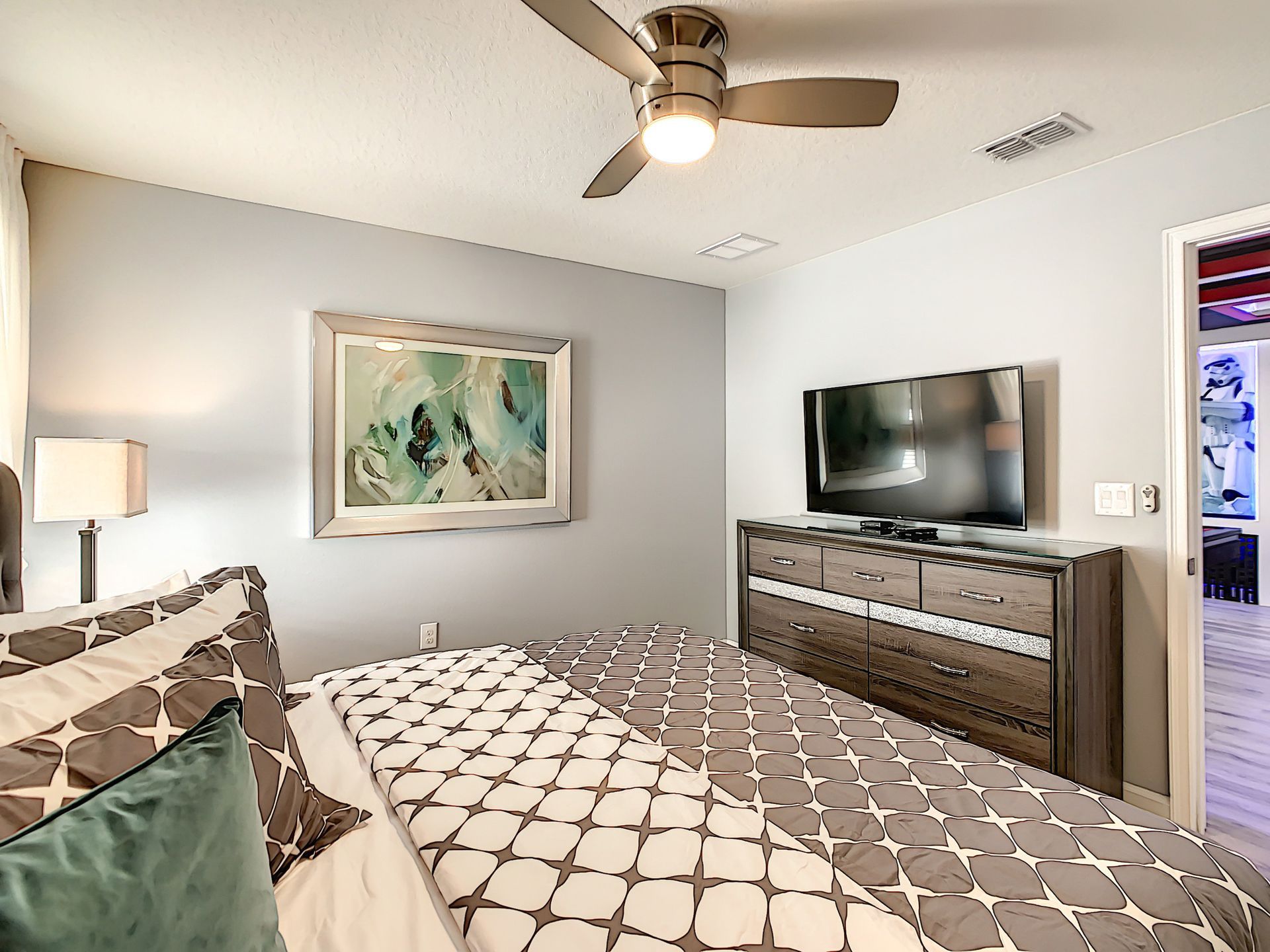 A bedroom with a bed , dresser , television and ceiling fan.