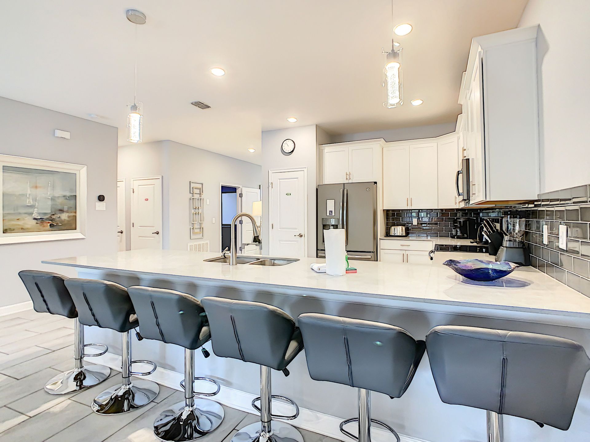 A kitchen with a long island , stools and a refrigerator.