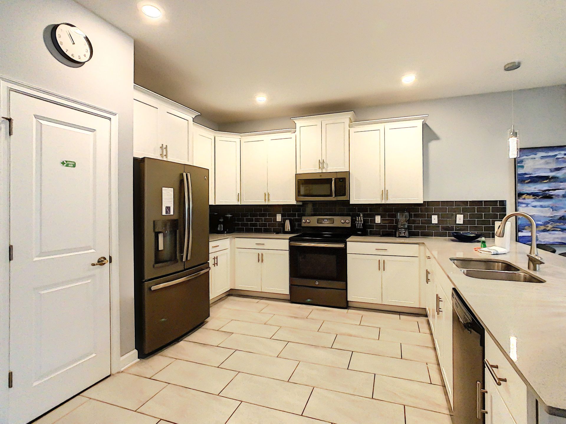A kitchen with white cabinets , black appliances , and a clock on the wall.