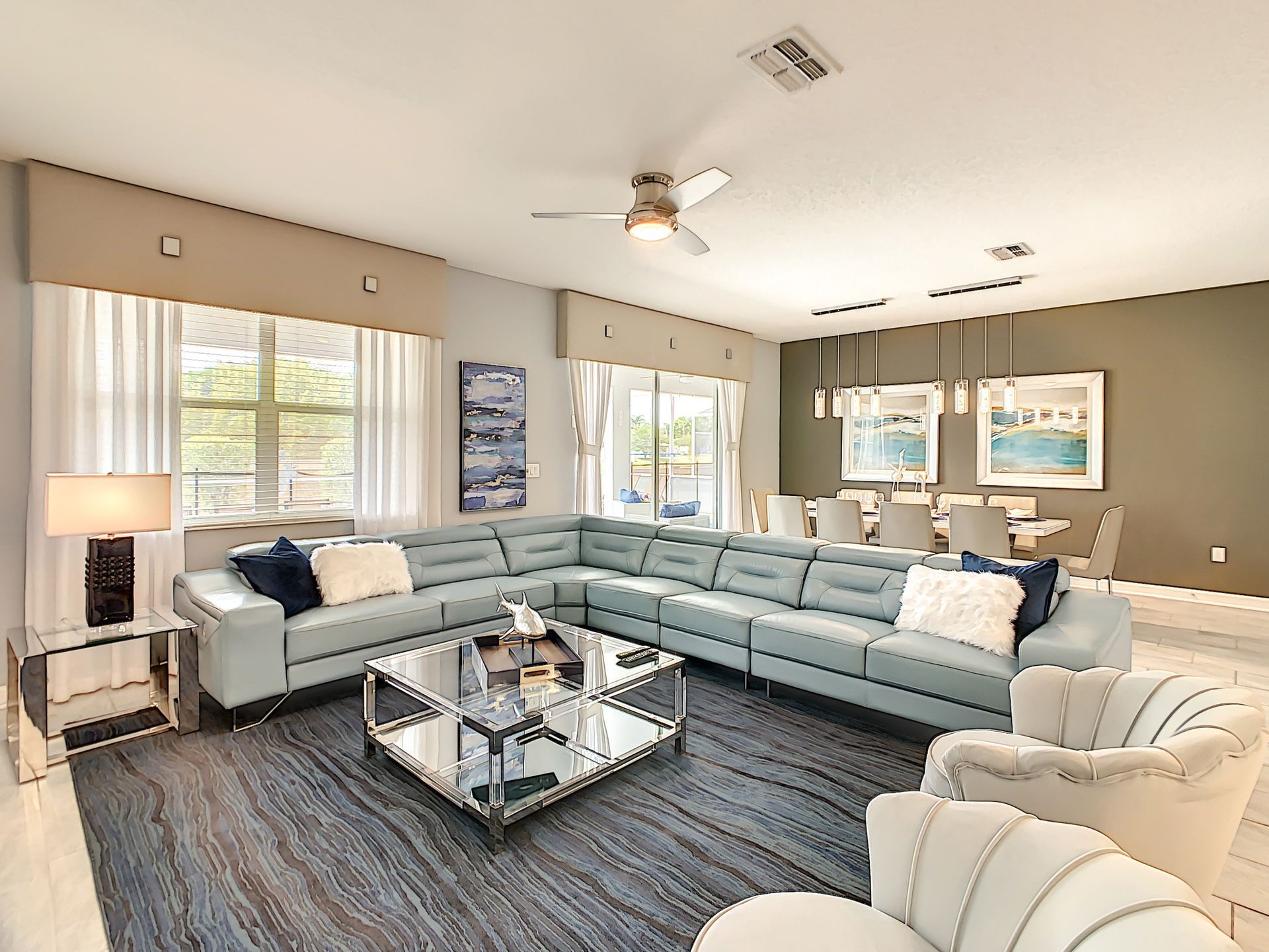A living room with a large sectional couch , chairs , a coffee table and a ceiling fan.
