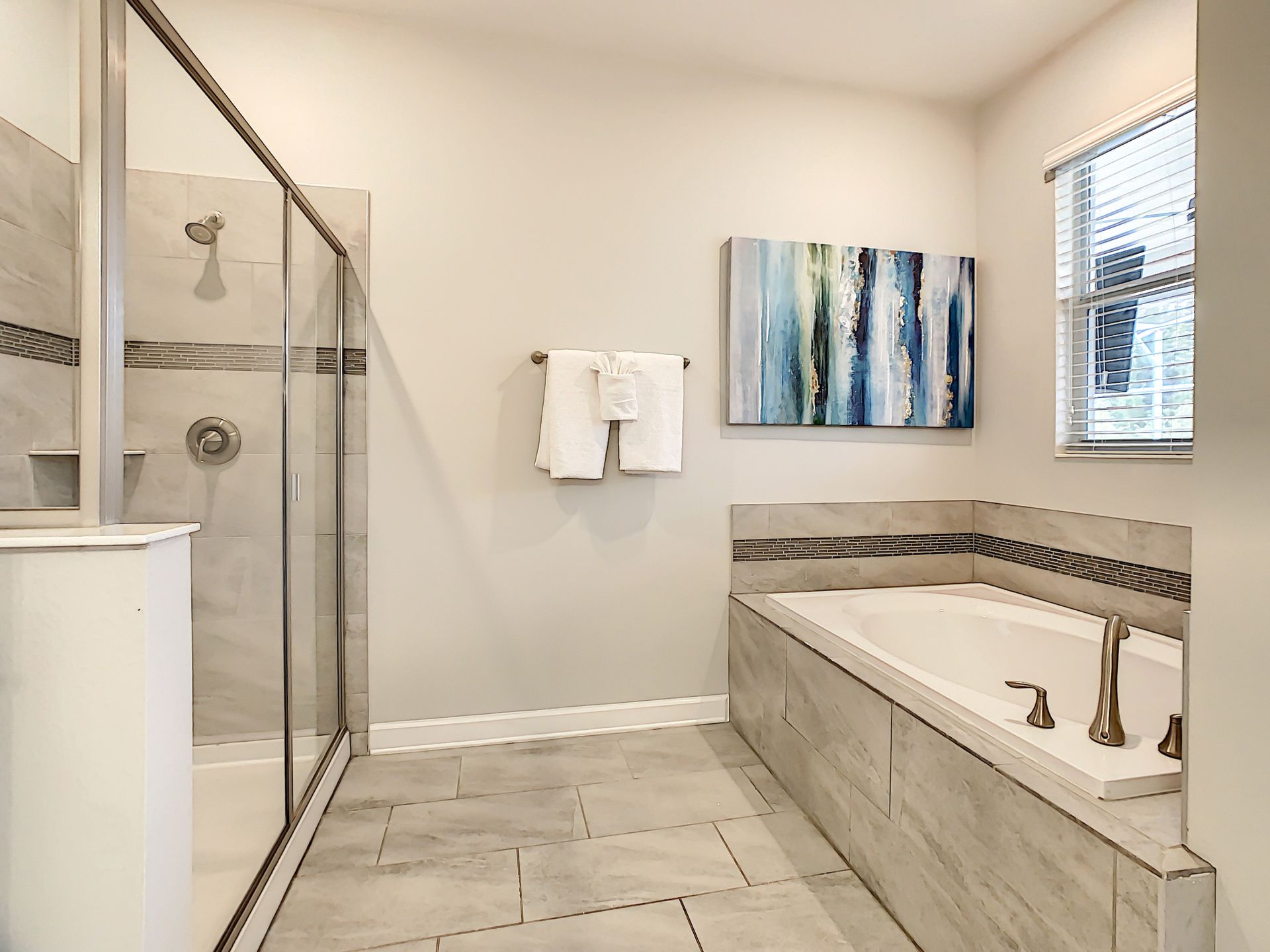 A bathroom with a tub , shower , sink and painting on the wall.