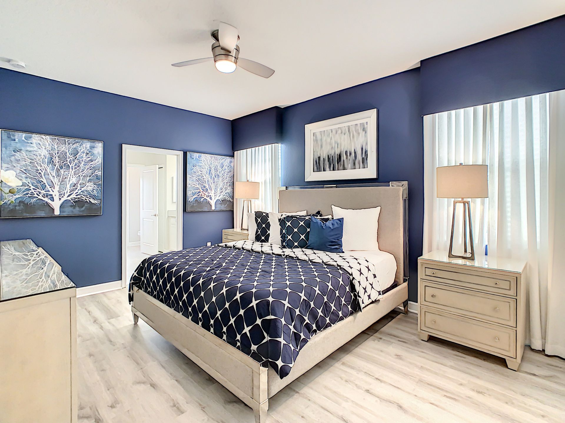 A bedroom with blue walls , a king size bed , nightstands , and a ceiling fan.