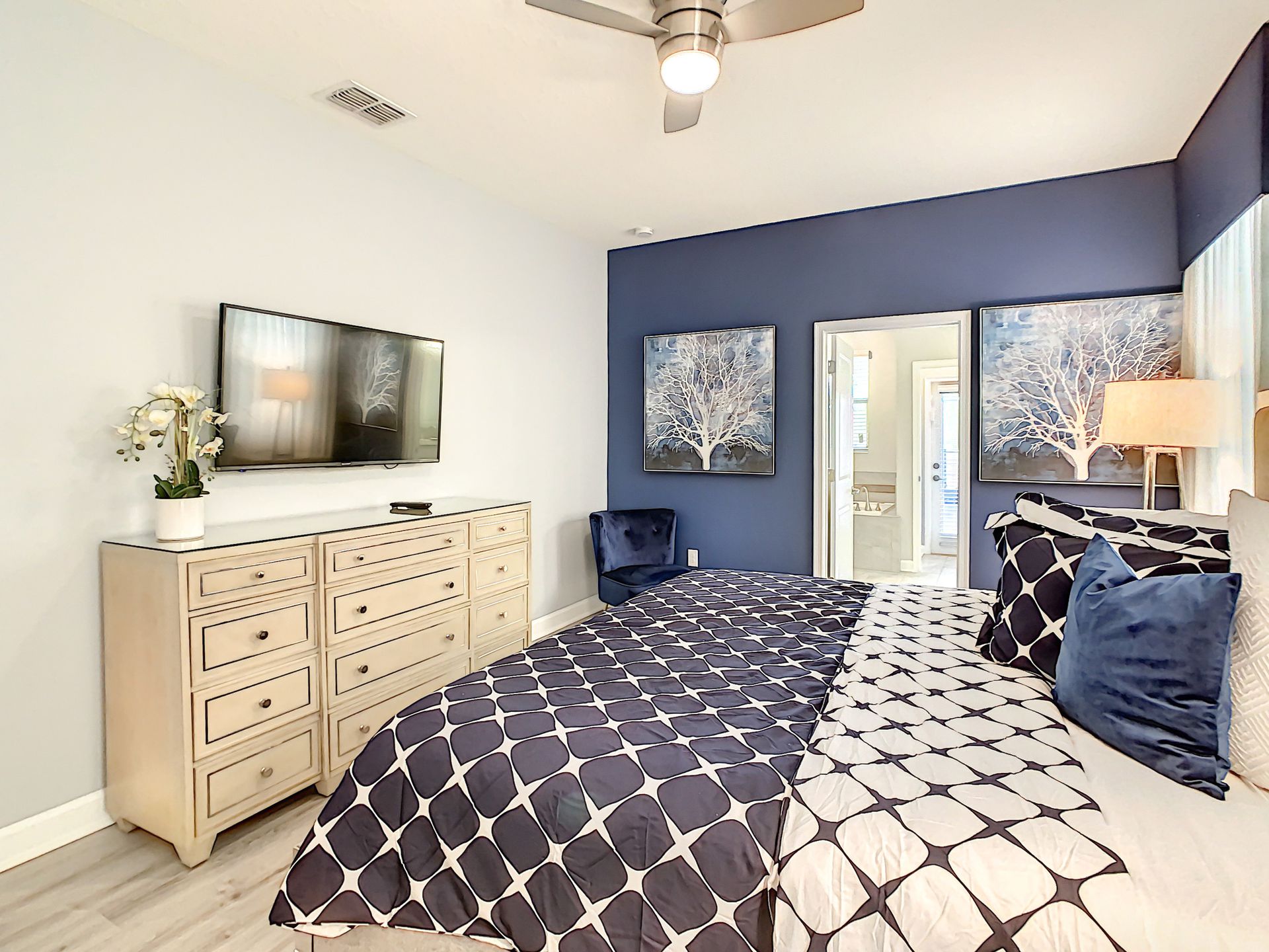 A bedroom with a bed , dresser , television and ceiling fan.