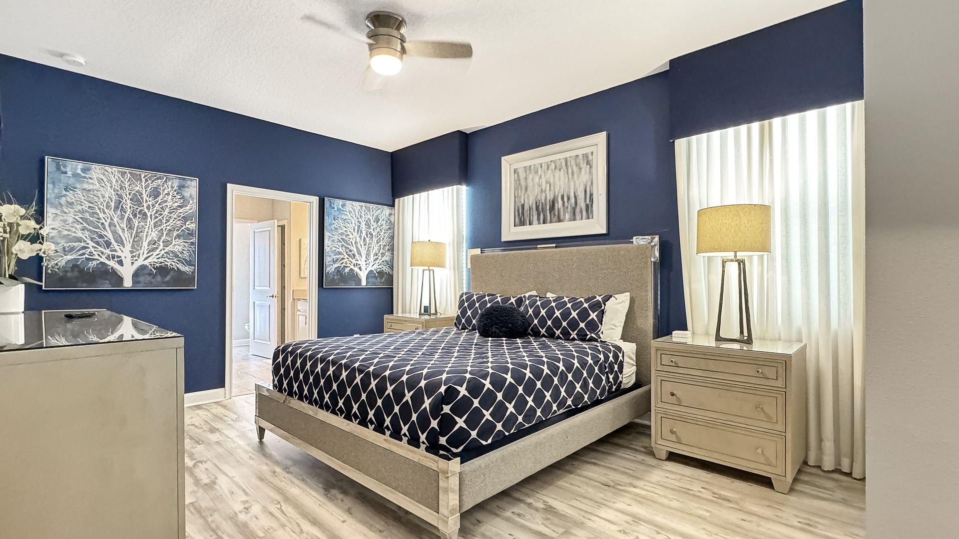 A bedroom with a king size bed , dresser , nightstand , and ceiling fan.
