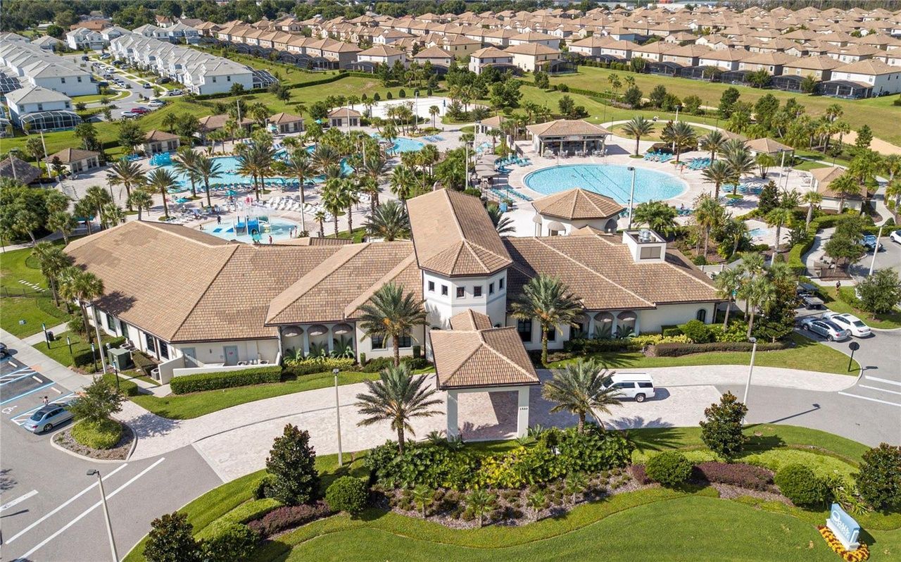 An aerial view of a large building with a pool in the background surrounded by palm trees.