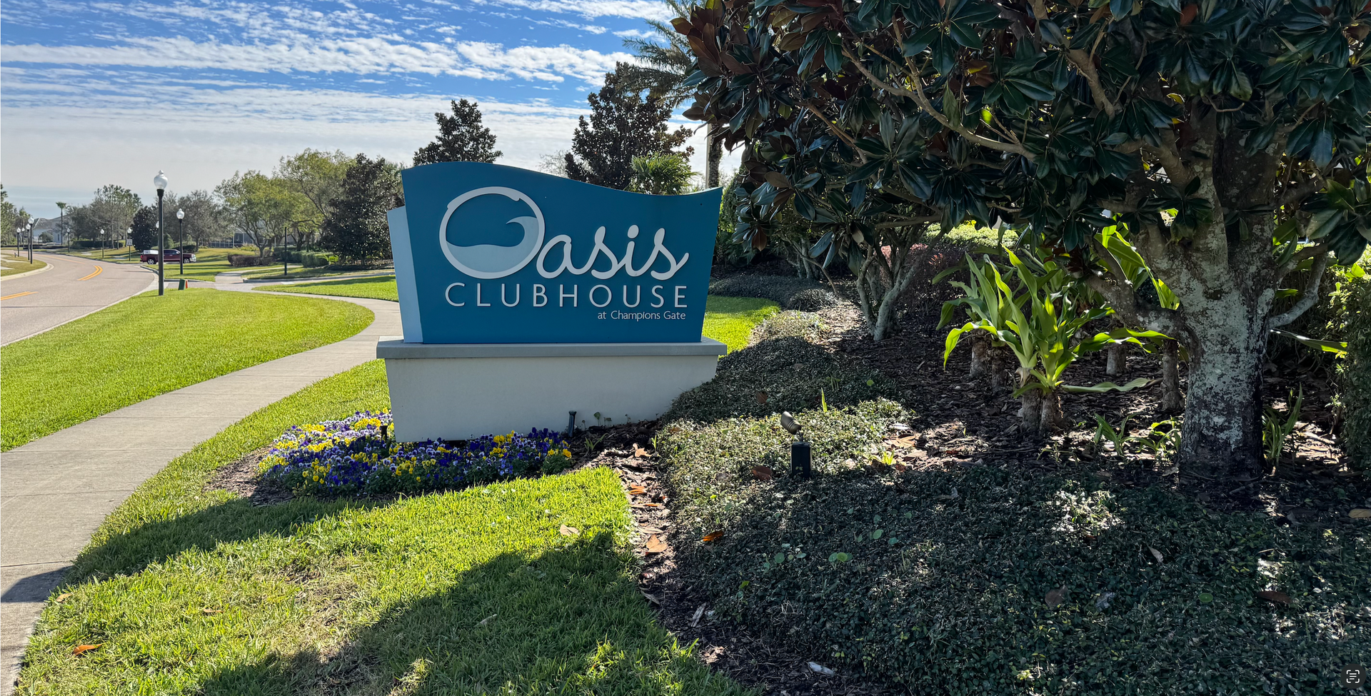A sign for the oasis clubhouse is sitting on the side of a road.