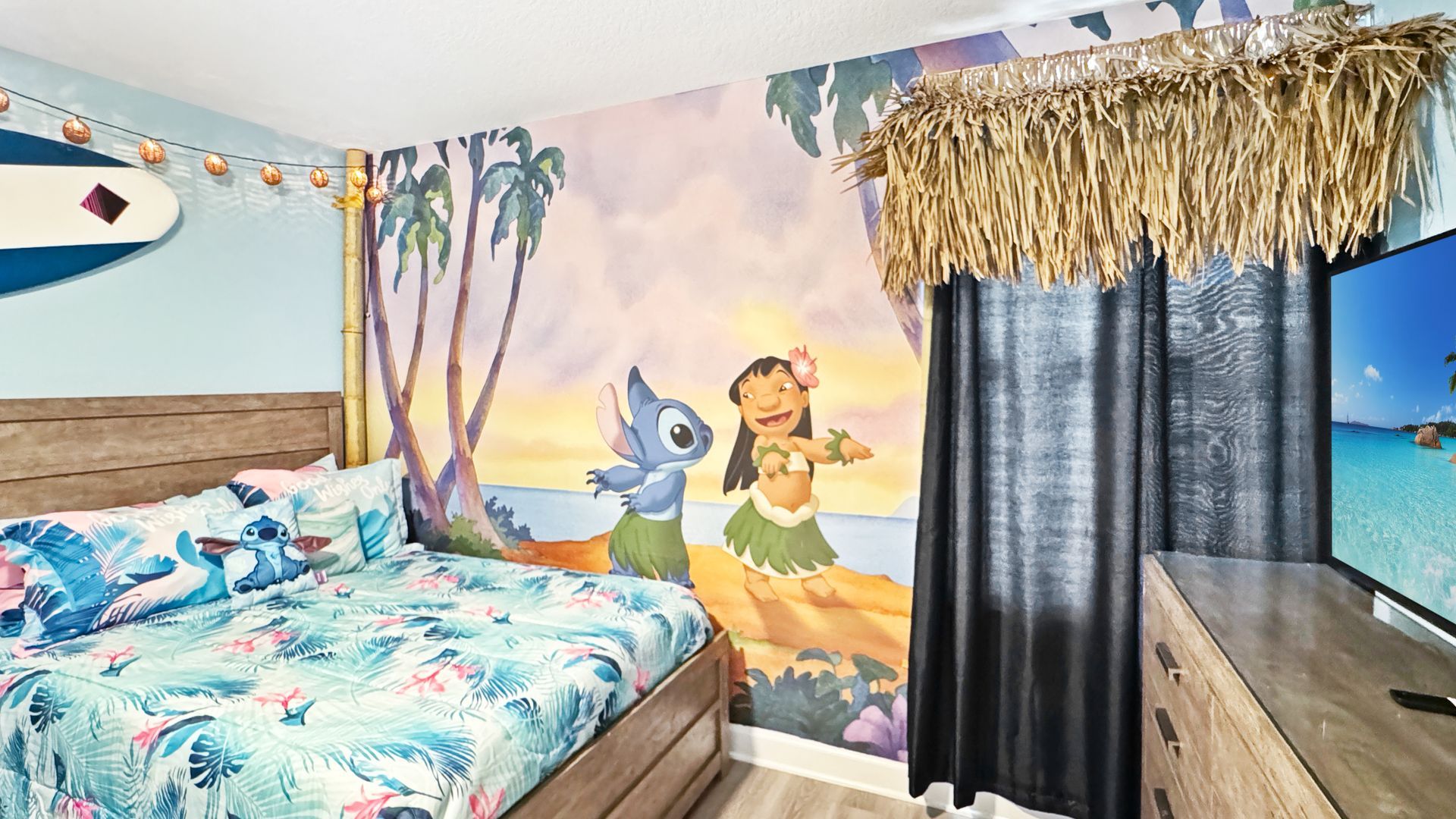 A bedroom with a bed , dresser , and television with a lilo and stitch mural on the wall.