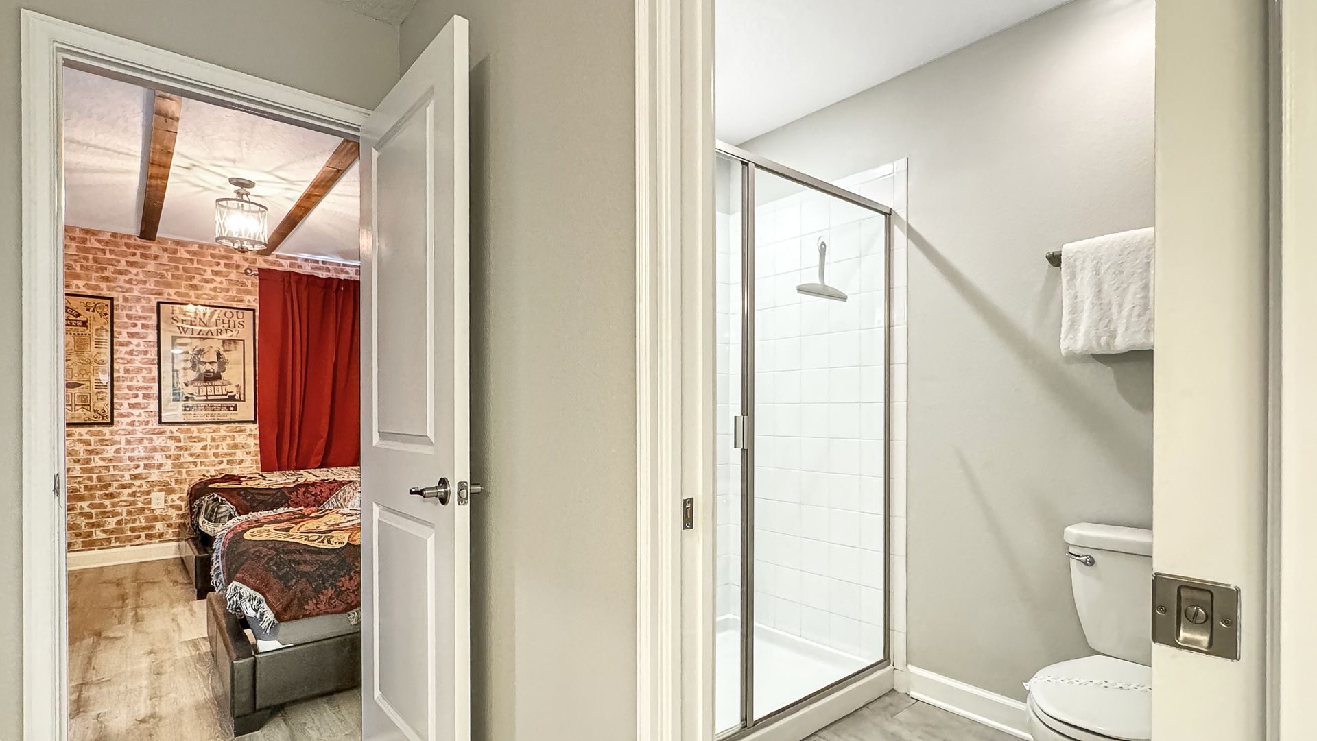 A bedroom with two beds and a bathroom with a walk in shower.