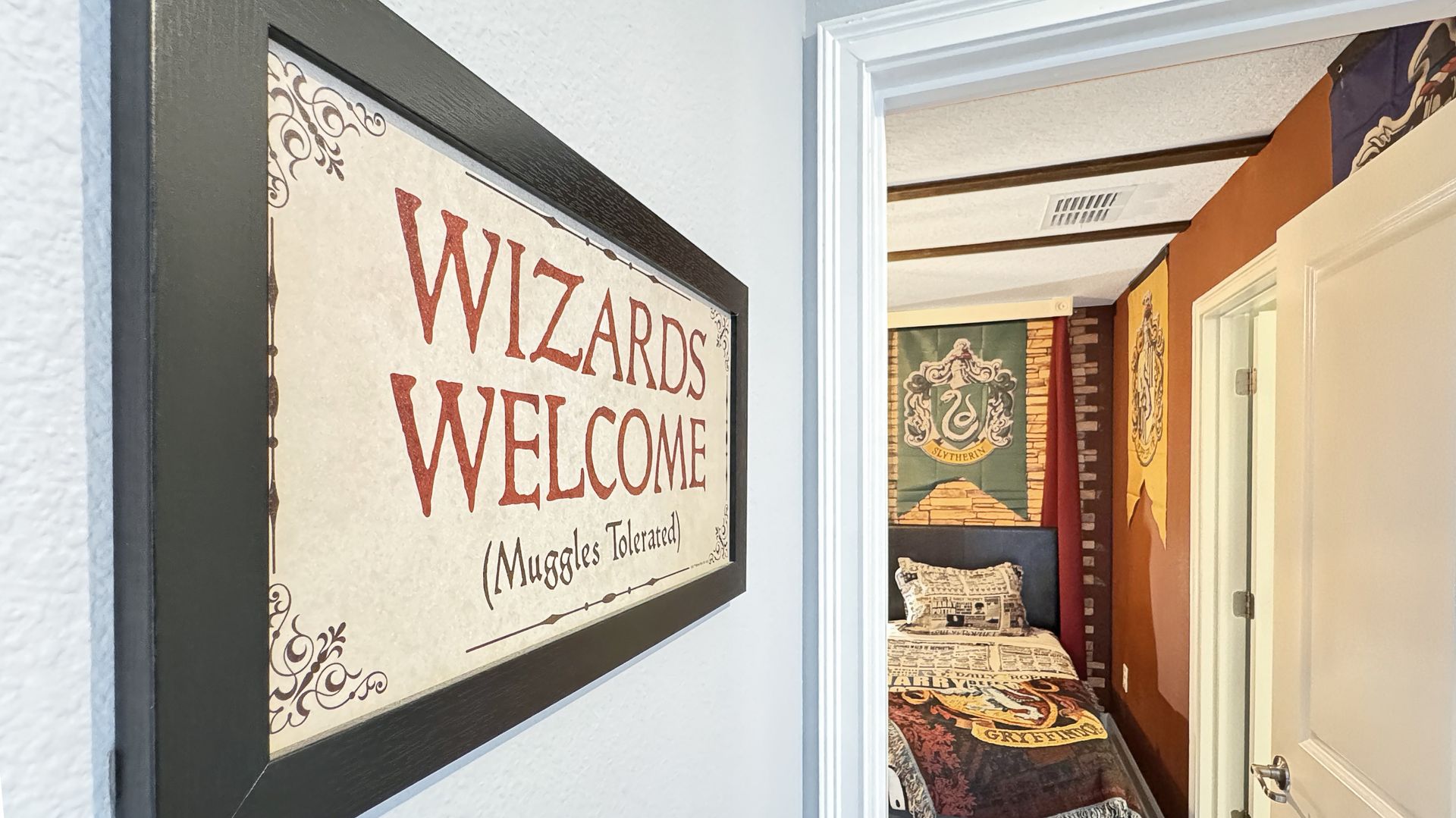 A framed sign that says `` wizards welcome '' is hanging on a wall next to a bedroom.