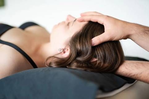 Person erhält Kopfmassage, liegt. Hände des Therapeuten auf dem Kopf. Schwarzer BH, Licht.