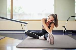 Eine Frau dehnt in einem Fitnessstudio ein Bein auf einer Matte.