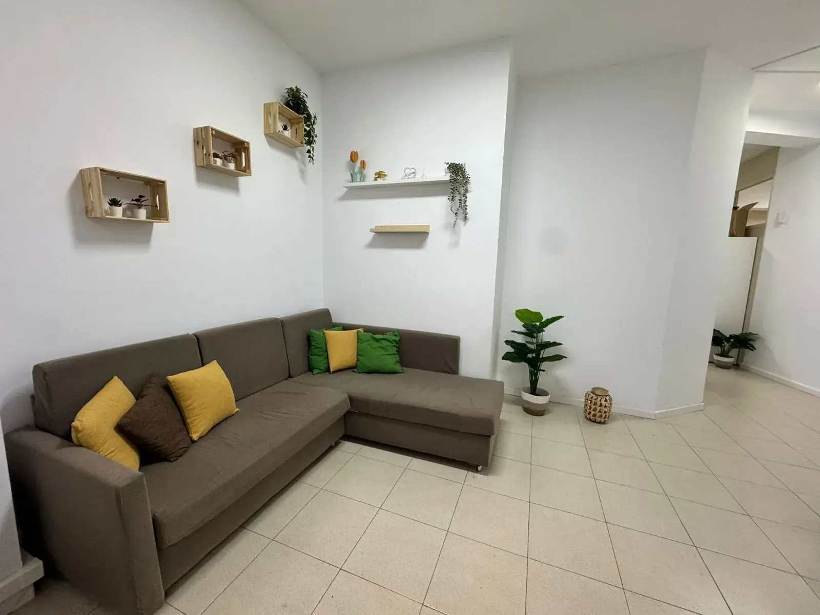 Una sala de estar con un sofá seccional marrón, paredes blancas, estantes decorativos y una planta.