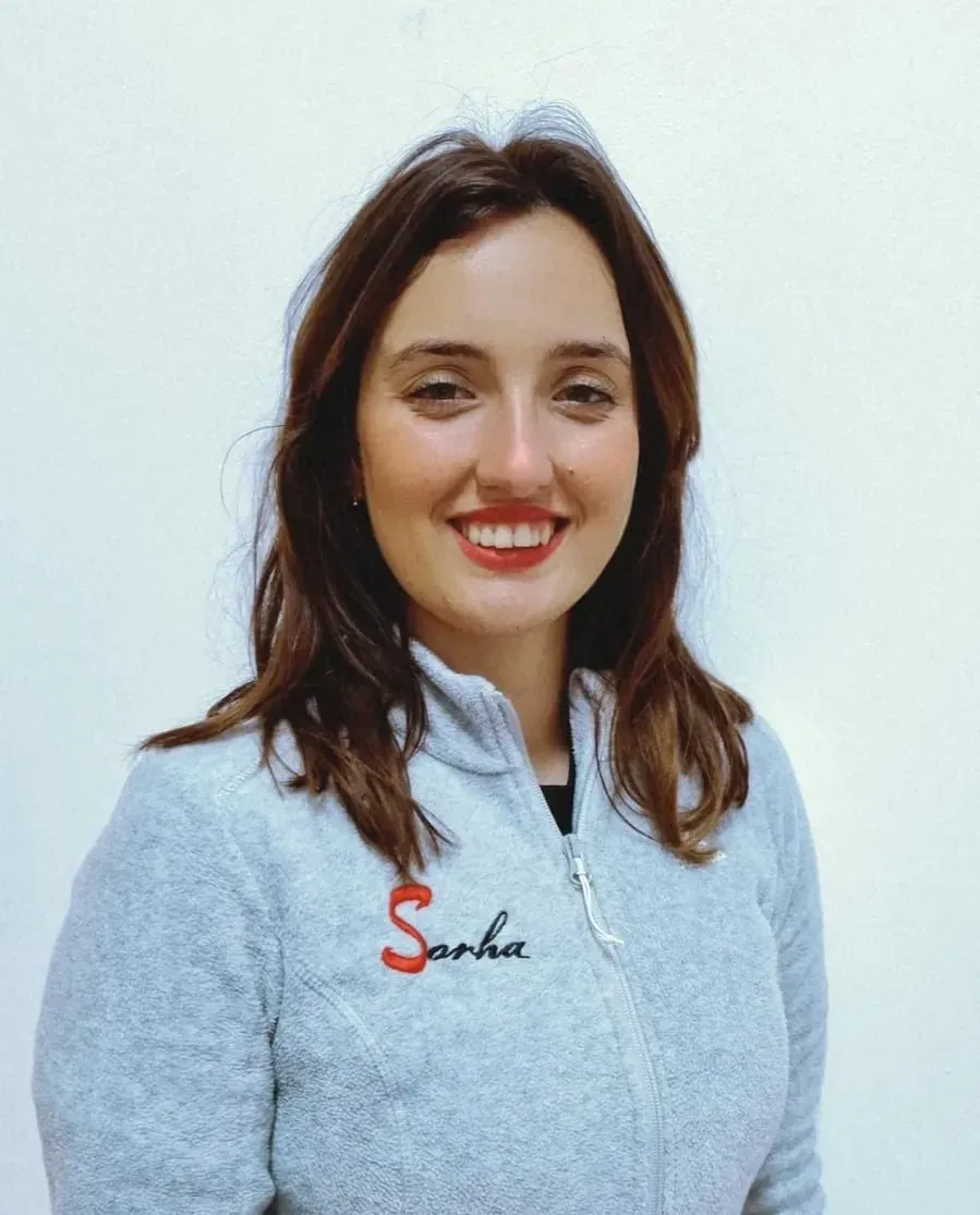 Una mujer de cabello oscuro sonríe, vestida con una sudadera gris con cremallera y la palabra 