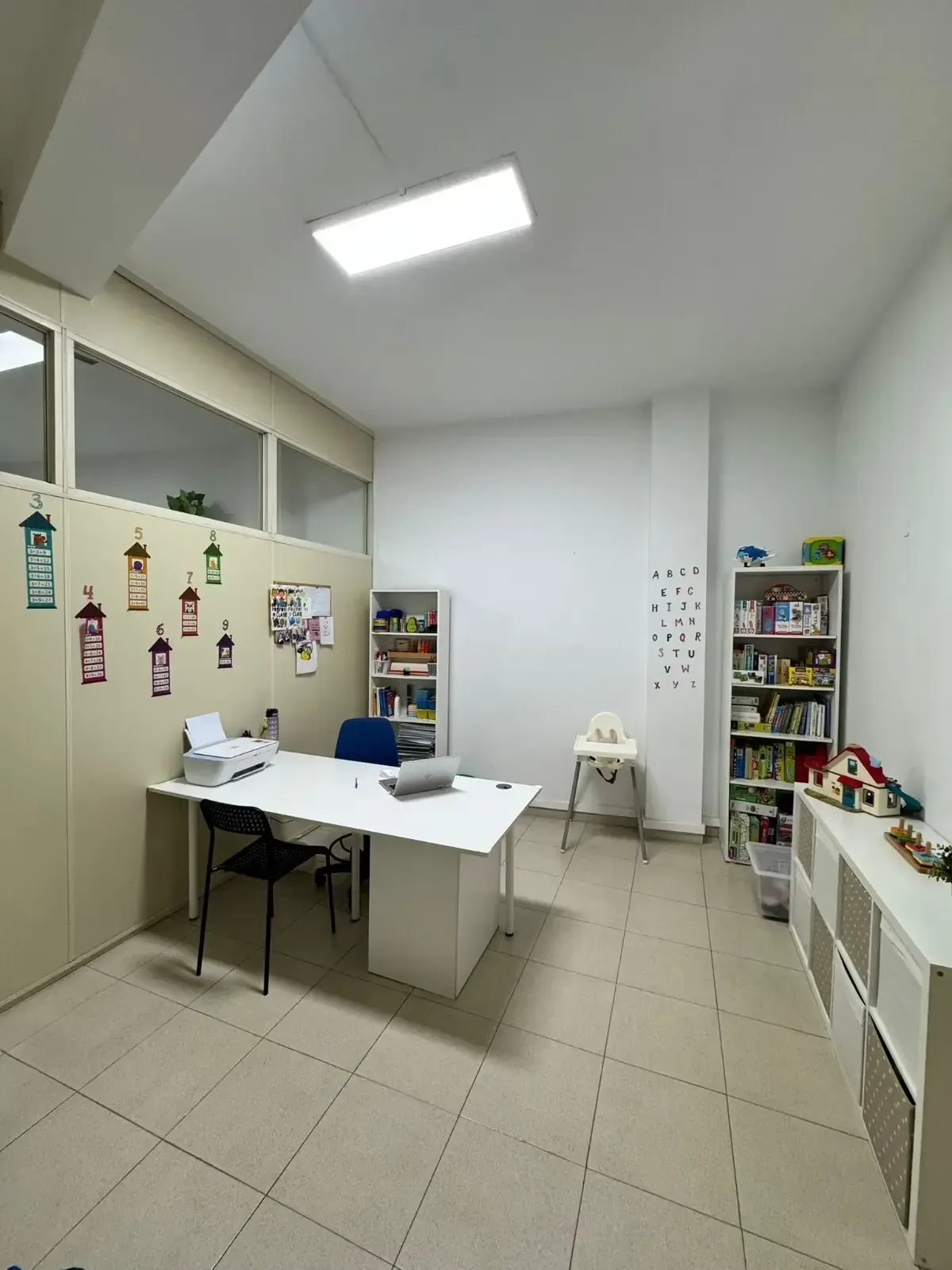 Espacio de oficina con paredes blancas, escritorio, estanterías y silla para niños.