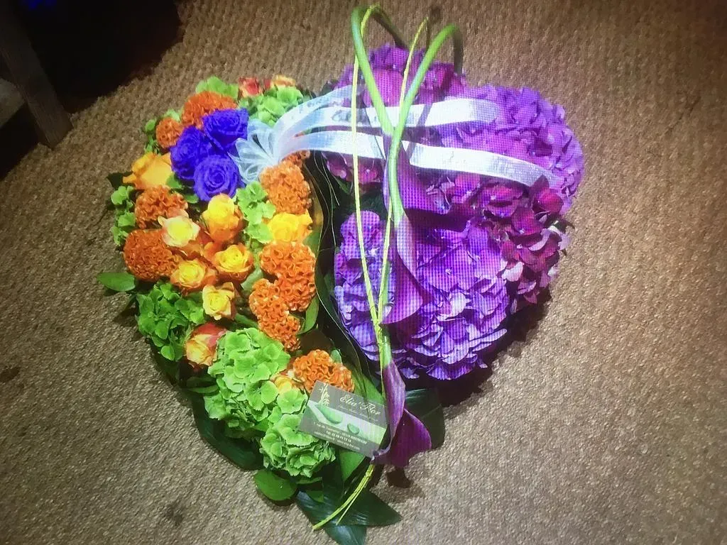 Composition florale, en forme de cœur, une partie violette et l'autre orange, bleue et verte