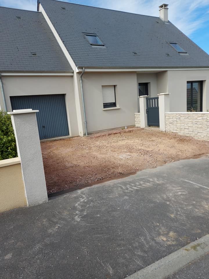 Maison grise avec garage, cour gravillonnée et portail gris.