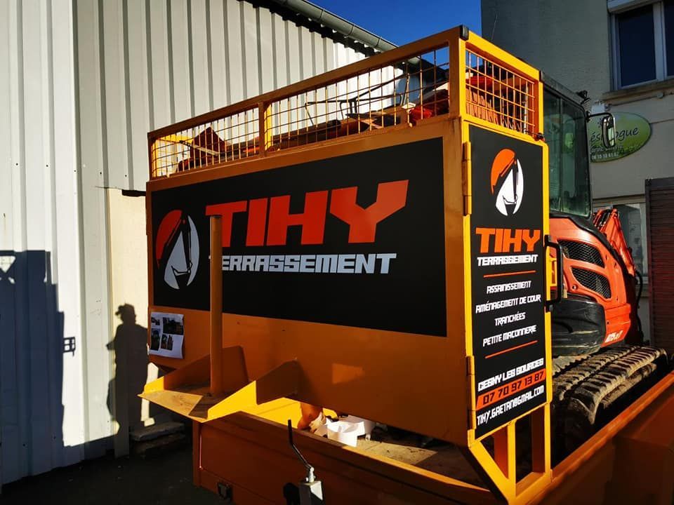 Remorque d'excavation TIHY orange avec logo noir, garée à côté d'un bâtiment.