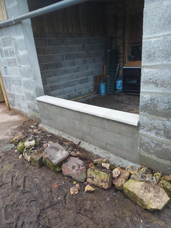 Vue extérieure d'une ouverture en parpaings avec un rebord en béton et une rangée de pierres en dessous.