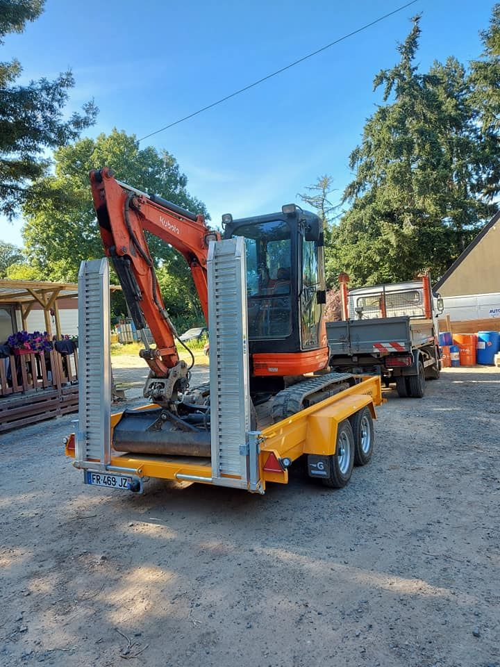 Une excavatrice orange sur une remorque jaune, avec un camion-benne attelé derrière.