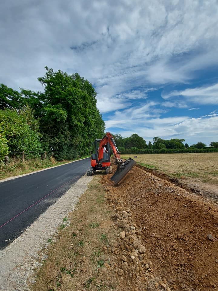 Une pelleteuse orange creuse la terre au bord d'une route. Journée ensoleillée avec des arbres.