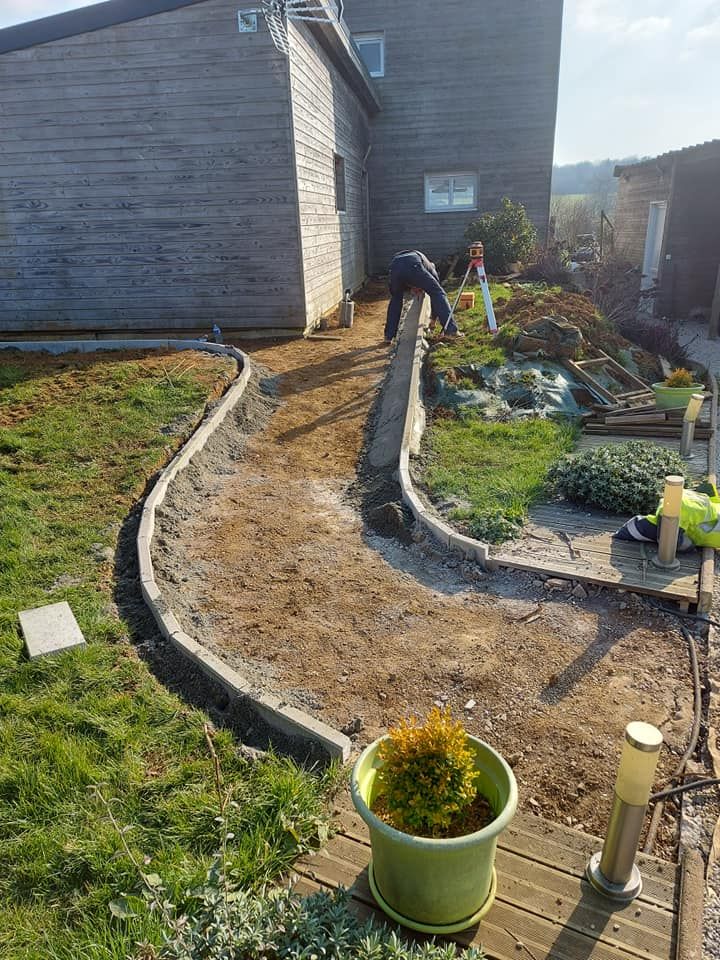 Une personne travaille à la construction d'un chemin en pierre à côté d'un bâtiment en bois et d'herbe verte.