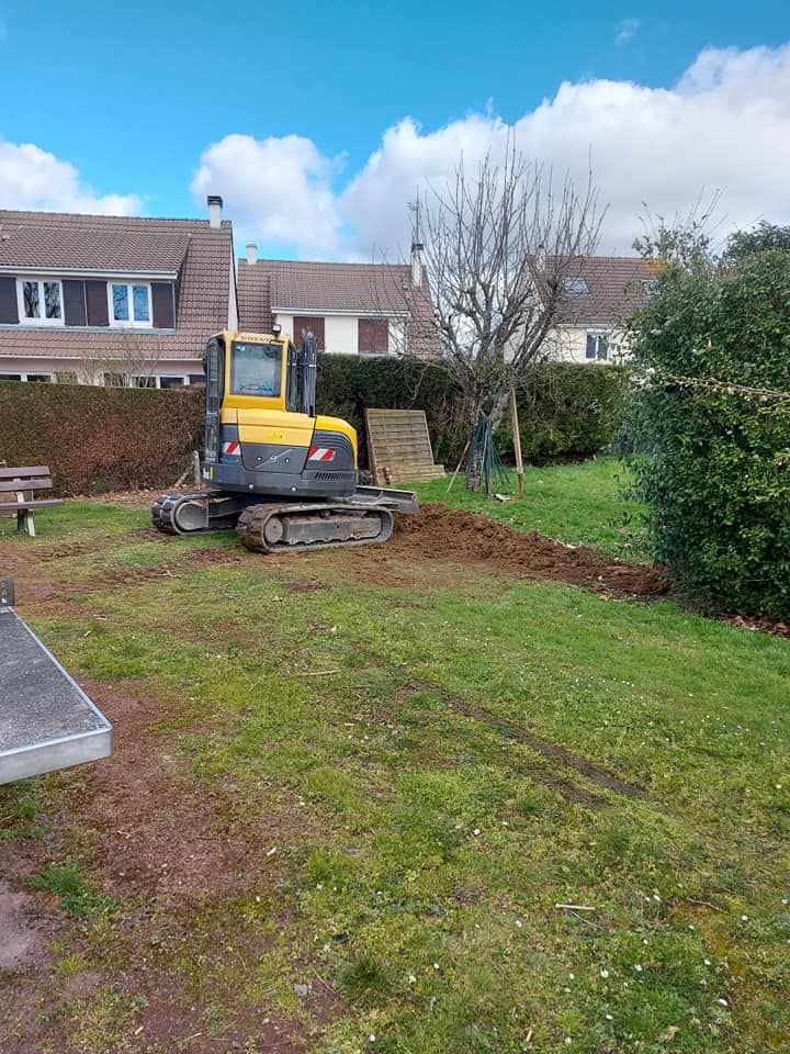 Une pelleteuse jaune creuse une tranchée sur une pelouse près des maisons. 