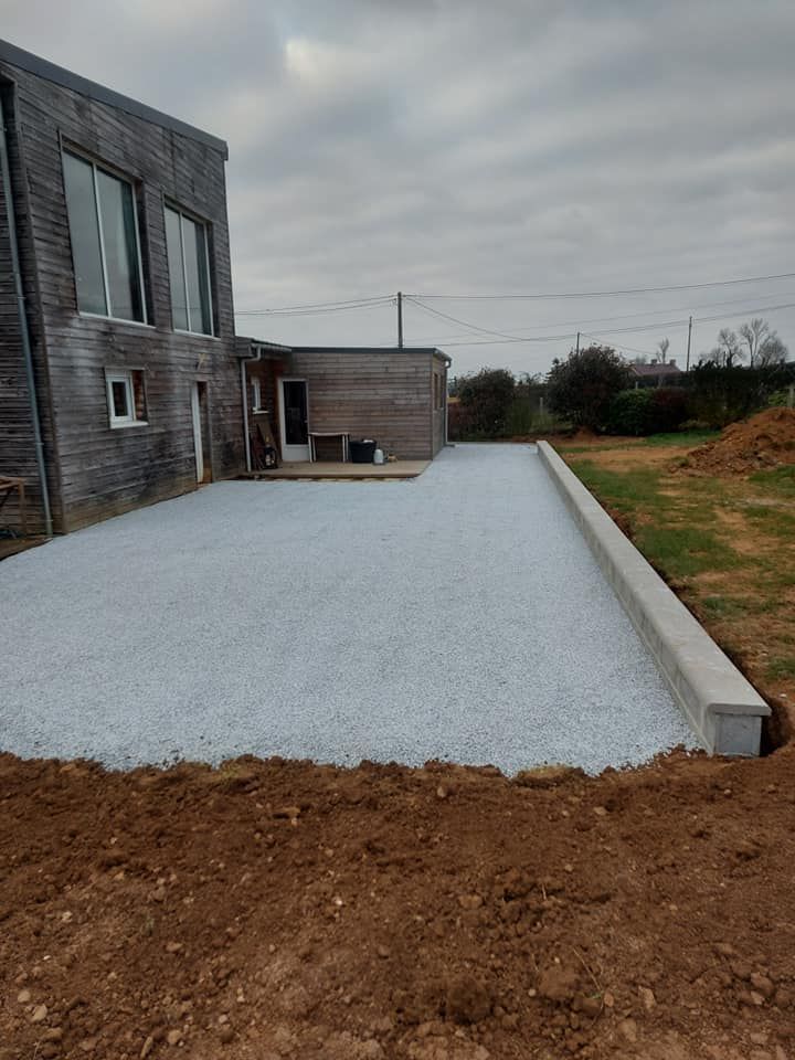 Terrasse en gravier jouxtant un bâtiment en bois et un mur de soutènement.