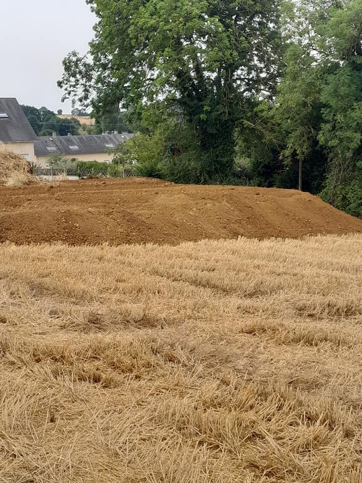 Tas de terre brune sur un champ de blé coupé, bâtiments et arbres en arrière-plan.