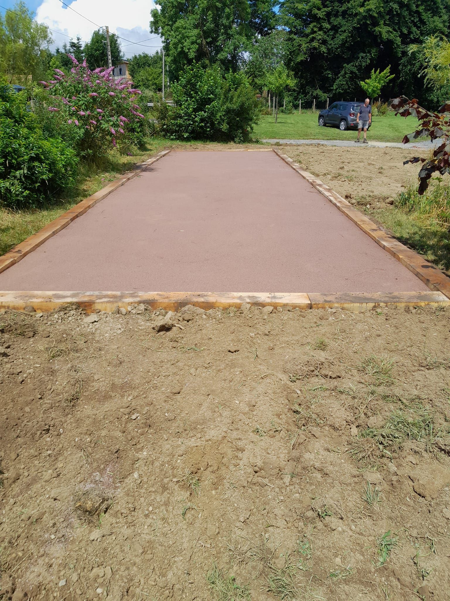 Terrain de pétanque nouvellement construit, avec une surface brun rougeâtre, délimité par des bordures en bois et entouré de terre.