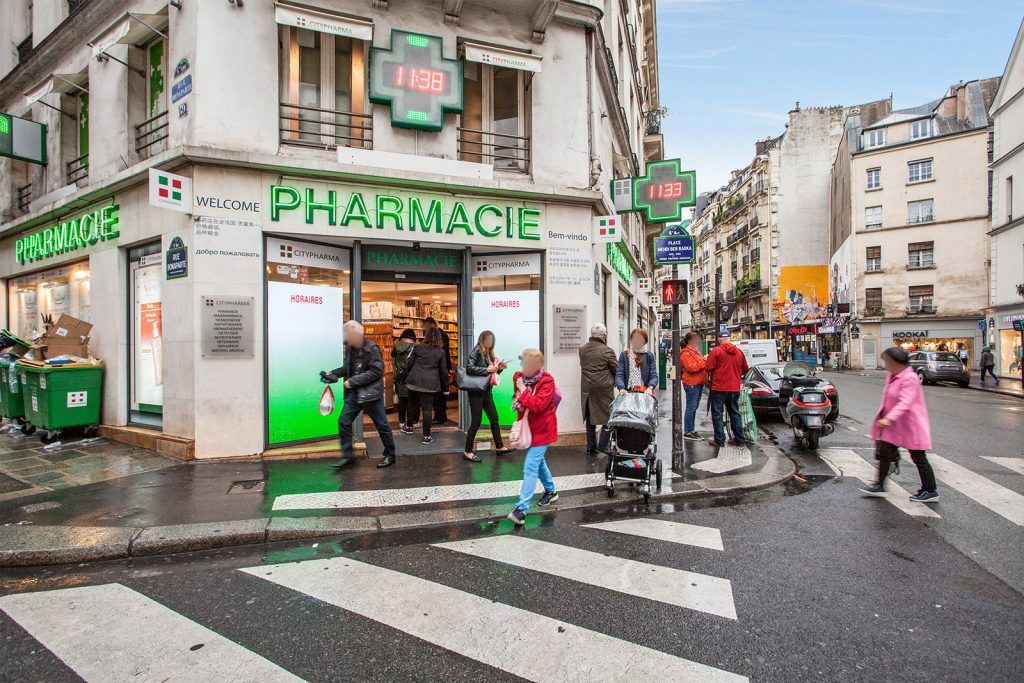 Coin de rue animé et pluvieux avec une pharmacie, des piétons et un passage piéton en plein centre-ville