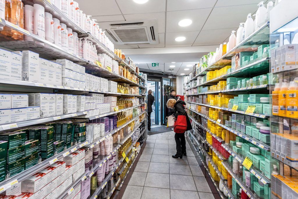Allée de la pharmacie avec des rayons de produits de toilette et une personne dans un sac rouge qui marche devant
