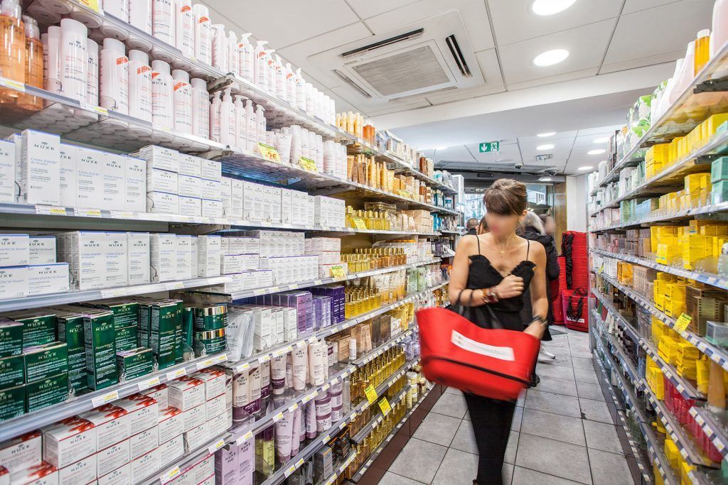 Une personne transportant un panier rouge dans une allée de magasin bordée d'étagères de produits