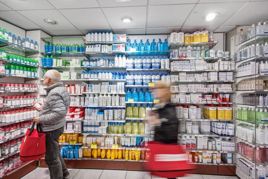 Des clients font leurs courses dans une allée bien éclairée d'un magasin rempli de produits de pharmacie