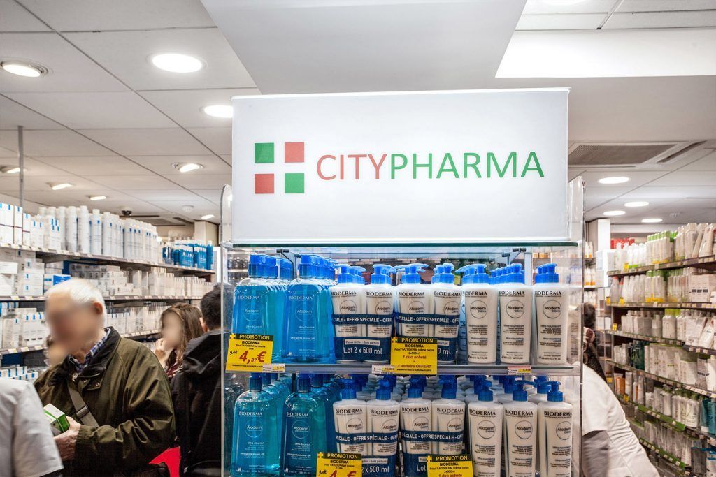 Allée de la pharmacie CityPharma avec présentoirs de produits bleus et une enseigne blanche au plafond