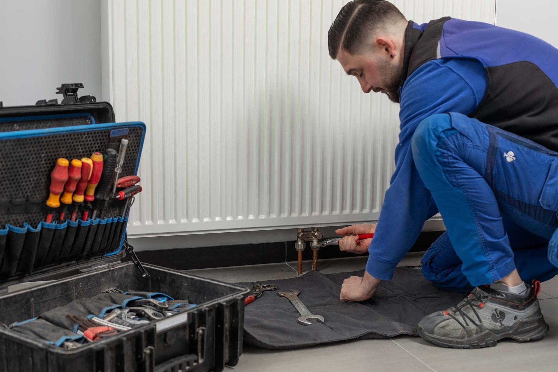Ein Mann kniet auf dem Boden und arbeitet an einem Heizkörper.