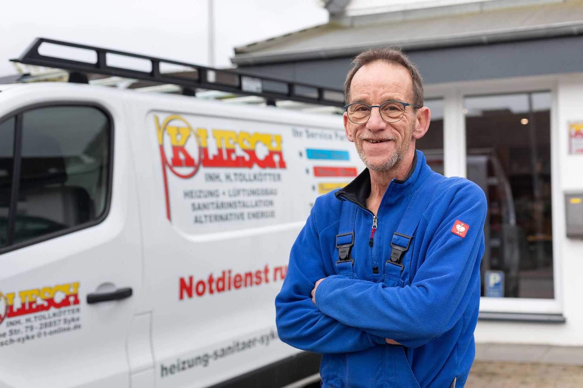 Ein Mann in einer blauen Jacke steht vor einem weißen Lieferwagen.