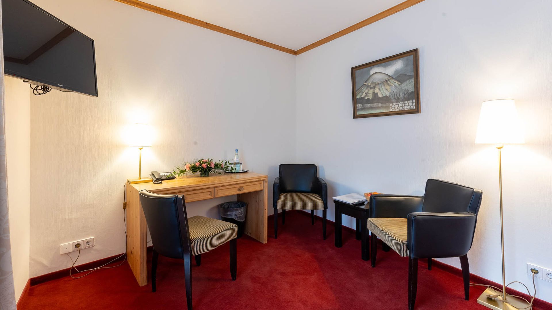 Ein Wohnzimmer mit zwei Stühlen, einem Schreibtisch und einem Flachbildfernseher.